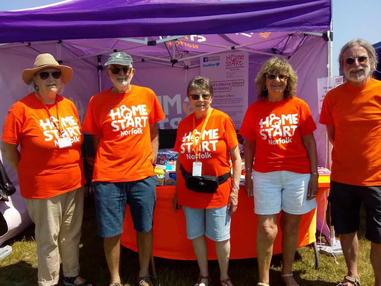 Five volunteers in orange home-start norfolk t-shirts standing in front of Home-start Norfolk Stand.